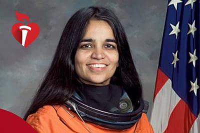 卡尔帕娜·舒拉穿着橙色太空服的肖像，背景是一面美国国旗